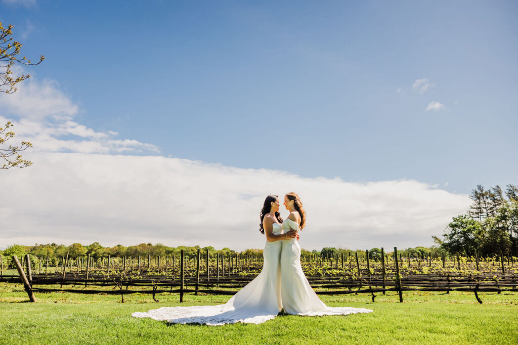 Two brides embrace in front of vineyard